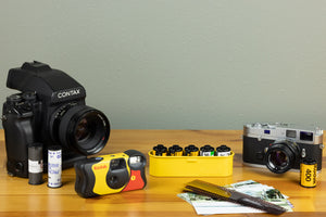 Contax and Kodak cameras on a table with various types of film and photos.