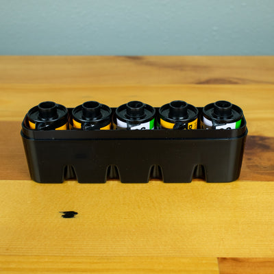 A top view of an opened black Japan Camera Hunter hard film case storing five 35mm films. 
