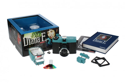 An open package containing the Lomography's Diana F+ camera, its flash, some colored gel flash filters, a hardcover book, and a manual. 
